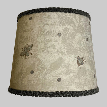 A lampshade with a beetle and spot pattern in an ocean color on a printed parchment background, with a dark grey gimp flat trim.